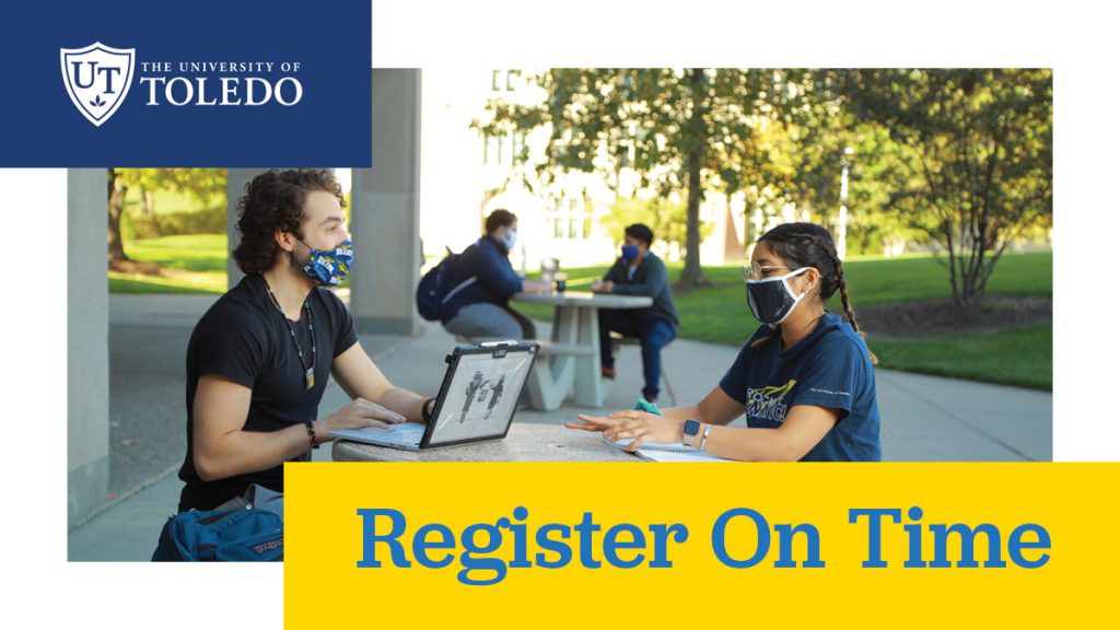 Students with masks sitting at tables outside Student Union with laptop and notebook