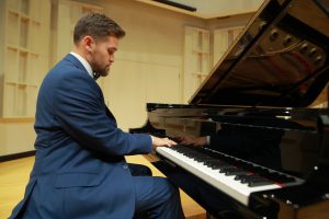 Male student wearing blue suit plays a Steinway piano on the Recital Hall stage