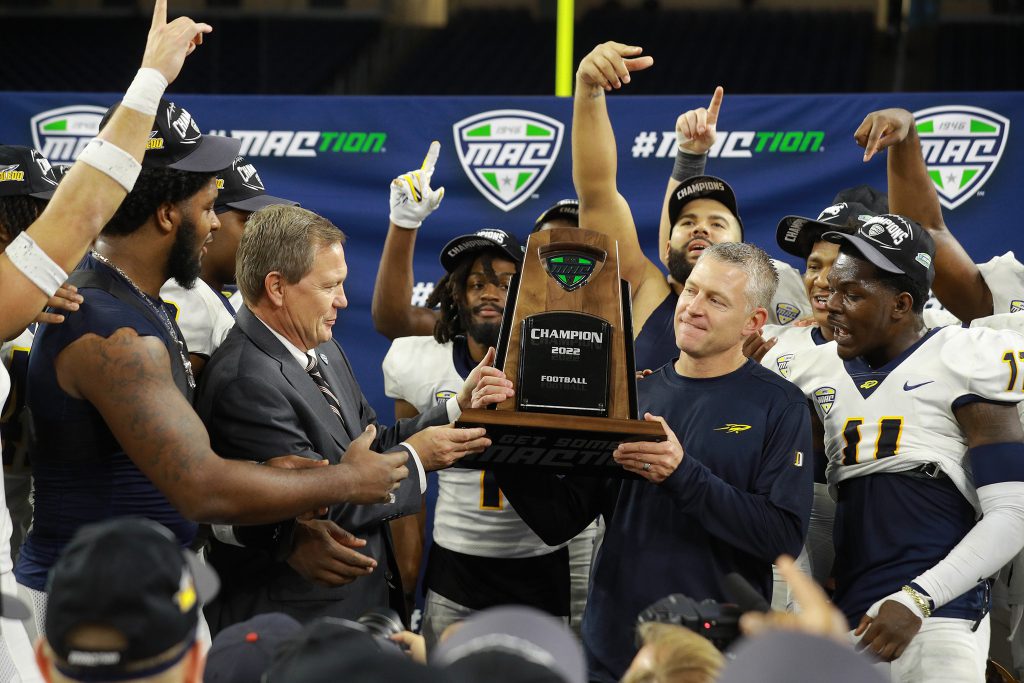 Coach Candle is presented MAC Trophy as football players cheer around him