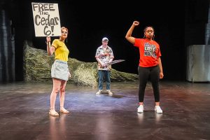 Three students standing on stage and holding signs