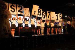 Students on a stage hold up signs showing how much money they raised during dance marathon