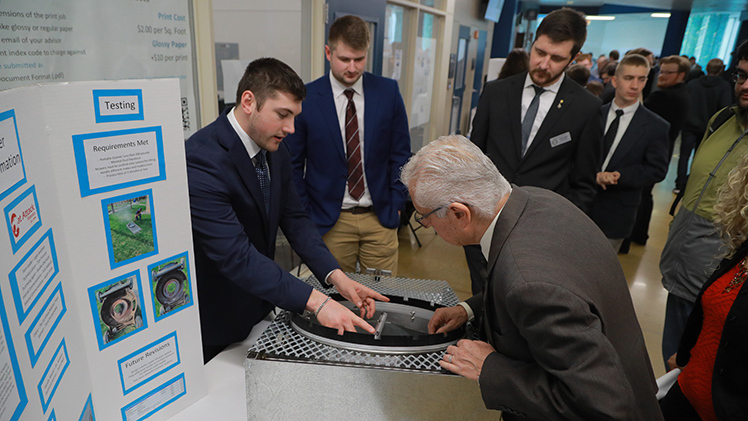 Bradley Eberhardt shows his team’s lawnmower cleaner to Hussein Abounaaj, a part-time professor evaluating projects, as teammates Logan Bradford and Tom Franczyk watch during the 2023 Senior Design Expo.