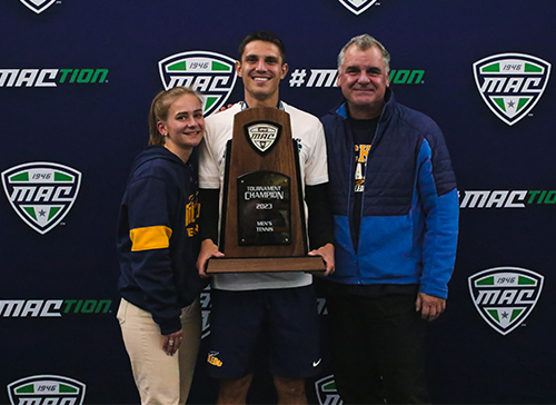 Senior men's tennis player Luis Kleinschnitz poses with the MAC 2023 Tournament Champion trophy, along with his girlfriend, Luise, and his father, Stephen
