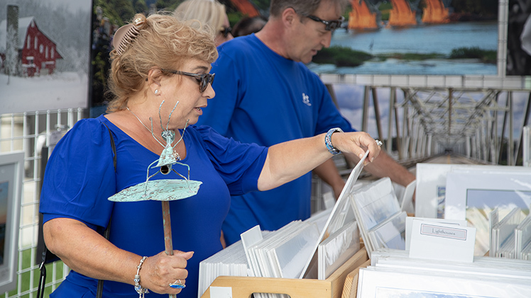 Julie Stobinski, from Temperance, Mich., looks through photographic prints Sunday at Jack Schultz’s booth at the 30th Art on the Mall at Centennial Mall.