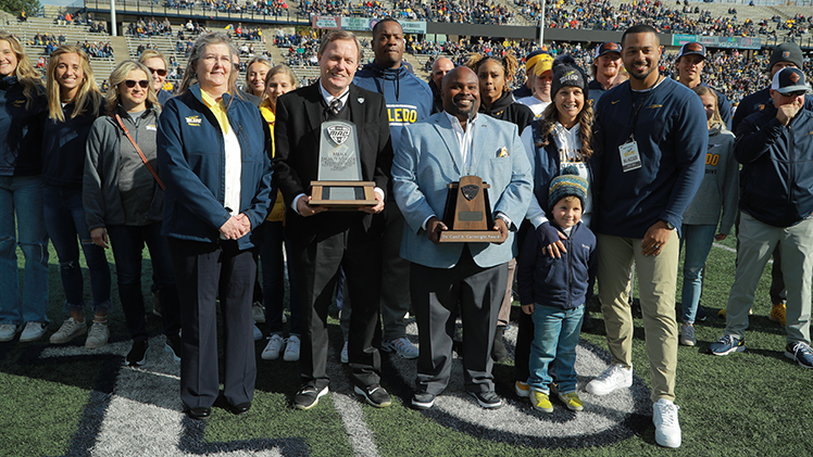 MAC Commissioner Jon Steinbrecher and Toledo Vice President and Director of Athletics Bryan B. Blair pose with other Rockets with the 2022 Cartwright Award on the field at the Glass Bowl Stadium before a game last year.