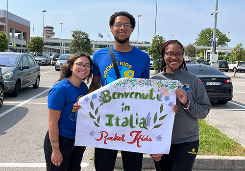 The three UToledo education students in the The University of Toledo’s Rocket Kids program pose with a sign in Italy.