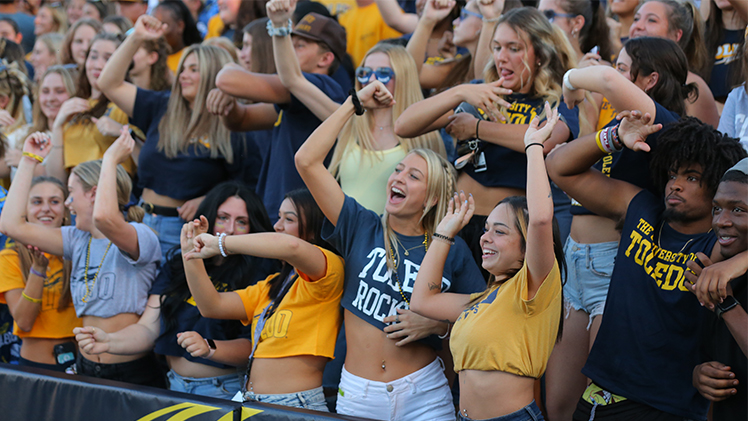 A crowd photo of cheering UToledo students in the stands at a home football game.