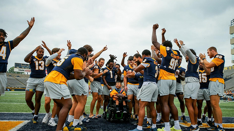 Photo of a group of University of Toledo football players sharing the joy of victory with a special needs student from Toledo Public Schools during the eighth annual "Victory Day" at the Glass Bowl on Saturday.