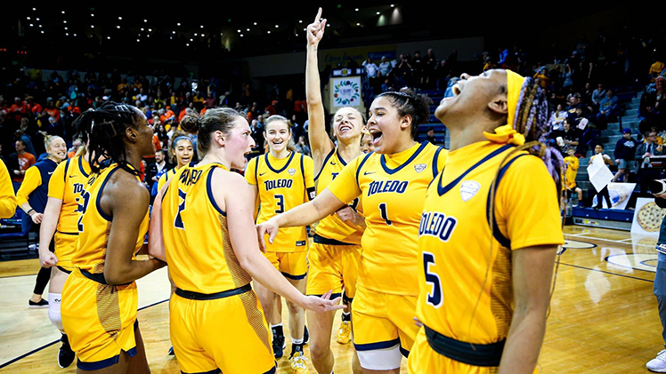 A group photo of the Toledo Women's Basketball Team celebrating a big win on the court.