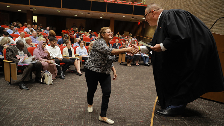Magistrate Judge Darrell A. Clay shakes the hand of Ignacia Bravo de Ojeda during a naturalization ceremony Friday inside The University of Toledo College of Law's McQuade Auditorium.