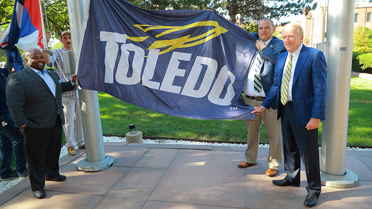 Vice President and Director of Athletics Bryan B. Blair, Toledo Mayor Wade Kapszukiewicz and UToledo President Gregory Postel pose with the Rocket flag during a Friday ceremony at One Government center in downtown Toledo.