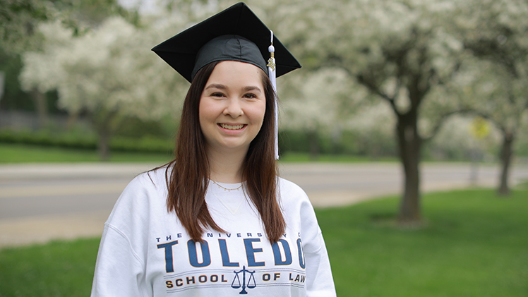 Feature photo of UToledo student Katie Zura, wearing a graduation cap and UToledo Law sweatshirt. She is in her second year of law school, having joined the College of Law through the 3+3 Accelerated program as a political science major at UToledo.