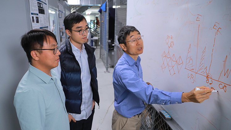 A photo of Dr. Yanfa Yan, a Distinguished University Professor in the Department of Physics and Astronomy, drawing on a white board with Dr. Xiaoming Wang and Yeming Xian watching.