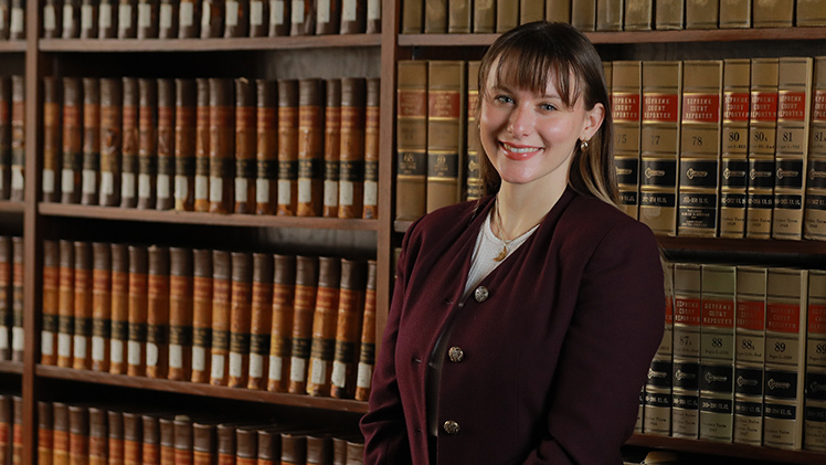 Feature photo of Lynn Hancsak, a second-year student at the College of Law, standing in front of books in a law library.