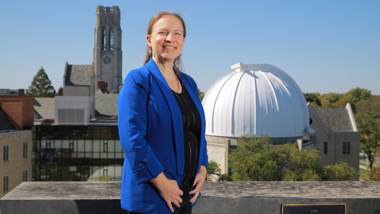 An outside feature photo of Dr. Anne Medling, an assistant professor the Department of Physics and Astronomy, on top of a UToledo campus building with the planetarium behind her.