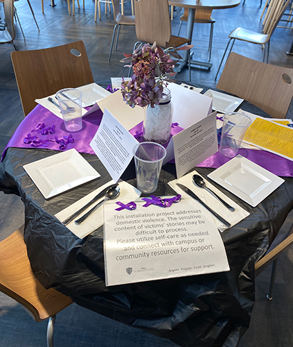 An "Empty Place at the Table” installation: a table set with a purple centerpiece and the narrative of an individual in Northwest Ohio who lost their life to domestic violence.