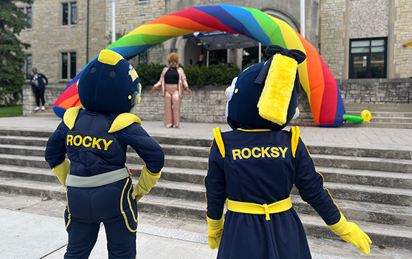 A photo of UToledo mascots Rocky and Rocksy in front of steps with an LGBTQA+ rainbow in front of them.