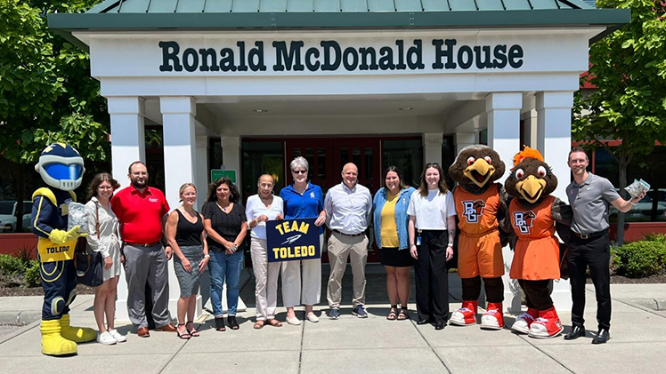 A group photo of members of The University of Toledo and Bowling Green State University athletic departments, school mascots and others in front of the Ronald McDonald House Charities of Northwest Ohio building.