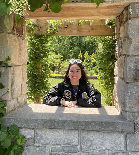 Photo of UToledo student Erica Sacoto framed by an opening in a stone wall with trees behind her.