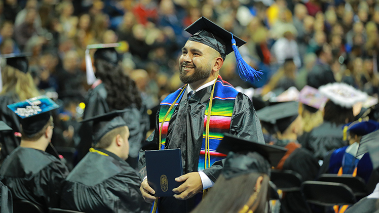 Photo of a UToledo male student in his graduation cap and gown standing up during a commencement ceremony.