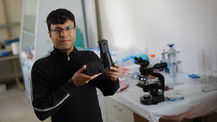 Feature photo of Dr. Aniruddha Ray, an assistant professor in the Department of Physics and Astronomy, holding a microscope.