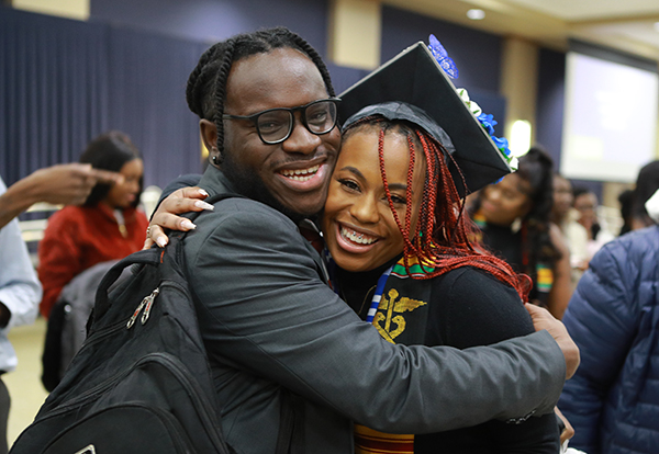 A man and a woman, who is dressed in a graduation cap and gown, hug during a Multicultural Graduation ceremony at UToledo.