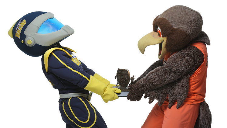 Photo of UToledo mascot Rocky and BGSU mascot Freddie each holding a side of a trophy that each is trying to pull to themselves.