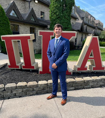 Photo of graduating engineering student Kyle Storer in front of the Pi Kappa Alpha fraternity letters.