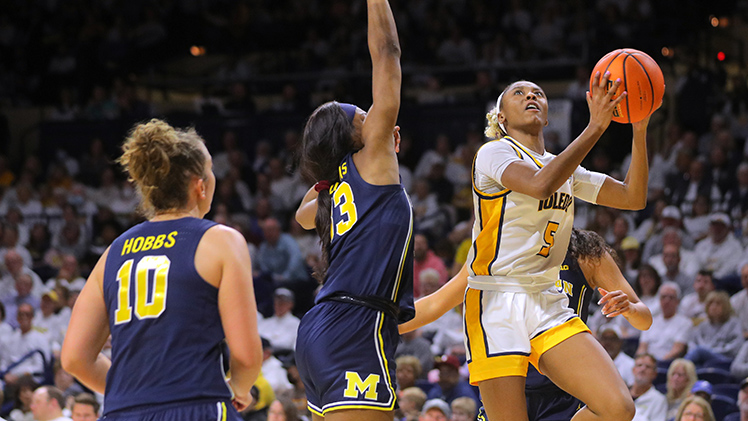 Photo of women's basketball player Quinesha Lockett against two Michigan defenders. She led all players with 20 points, her fourth consecutive 20-point game.