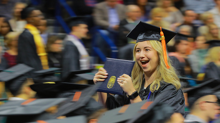 Lindsey Shaffer excitedly raises her diploma holder as she walks back to her seat after receiving a bachelor of science degree in construction engineering technology during the afternoon fall commencement ceremony on Saturday, Dec. 16, in Savage Arena.