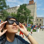 Photo of female UToledo student looking at a solar eclipse through special glasses on Aug. 8, 2017.