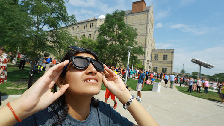 Photo of female UToledo student looking at a solar eclipse through special glasses on Aug. 8, 2017.