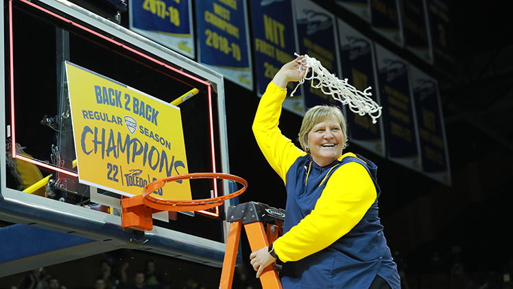 Toledo women's head basketball coach Tricia Cullop stands on a ladder and waves a cut basketball net in the air after winning the 2023 MAC Tournament championship. 