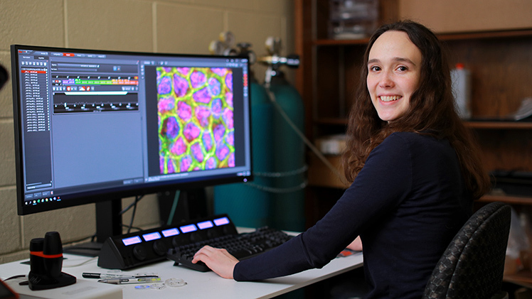 Sophia Durham poses at a computer in the research lab of Dr. Rafael Garcia-Mata, a professor who explores the mechanisms of cell behavior in the Department of Biological Sciences.