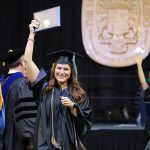 A female UToledo student holds up her diploma during a commencement ceremony as exits the stage.