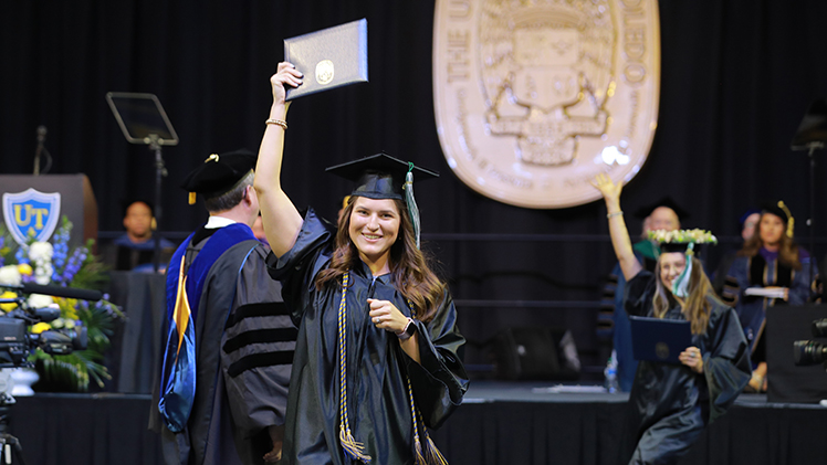 A female UToledo student holds up her diploma during a commencement ceremony as exits the stage.