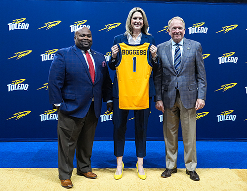 Ginny Boggess, who was officially introduced as the head women's basketball coach at The University of Toledo at a press conference on Tuesday, poses with a Rockets jersey along with The University of Toledo President Gregory Postel and Vice President and Director of Athletics Bryan B. Blair.