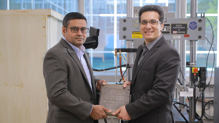 Dr. Joseph Lawrence, associate professor in the Department of Chemical Engineering, and Dr. Meysam Haghshenas, assistant professor in the Department of Mechanical, Industrial and Manufacturing Engineering, show off a sample of the material used to replace an arrestor arm at the Poe Lock inside Haghshenas’ Failure, Fracture and Fatigue Laboratory.