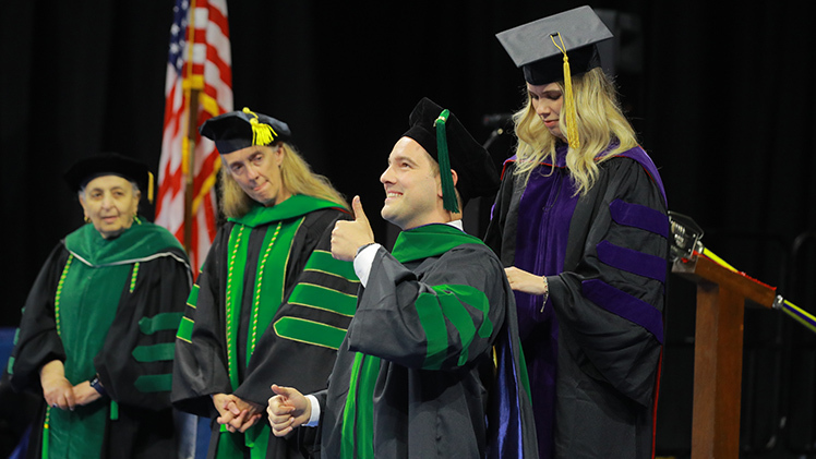 Catalin Dragomirescu gives the thumbs-up after being hooded Friday during the College of Medicine and Life Sciences spring commencement ceremony in Savage Arena.