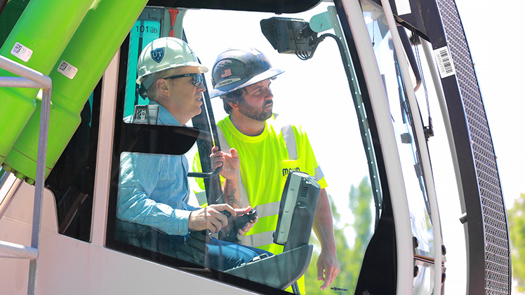 UToledo Interim President Matt Schroeder, wearing a white construction helmet, sits inside the operator's cab of a material handler as he is about to officially begin the demolition of Palmer Hall on Main Campus.