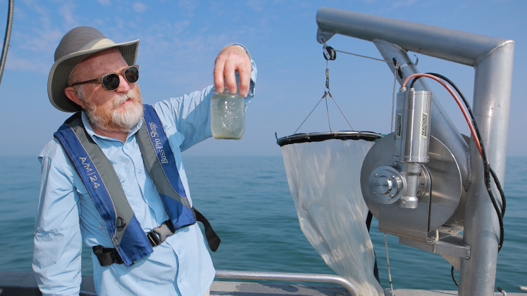 Dr. Thomas Bridgeman, professor of ecology and director of The University of Toledo Lake Erie Center, is on a boat as he examines a glass of water from Lake Erie.