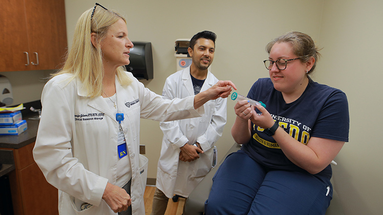 Jennifer Gilmore, left, a clinical research manager in the UToledo Department of Medicine, demonstrates one of the lung screening devices that will be used in the Great Lakes Aerosol Monitoring Research Study as Katie Behrens, a research clerical assistant in the Department of Medicine, plays the role of a patient. The study aims to follow 200 individuals from Lucas, Ottawa and Sandusky counties over the next of five years.