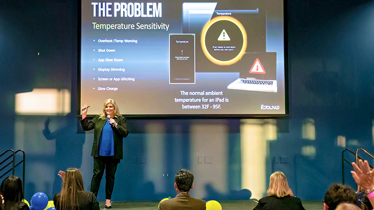 A photo from the 2023 "Pitch & Pour" event with a woman on stage making a presentation to a large group of people. 