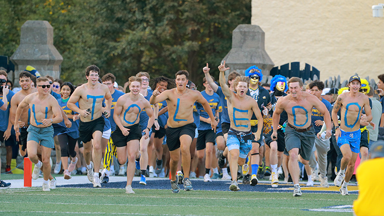 Several shirtless male students, each with a letter painted on their chest that spells out U-T-O-L-E-D-O run onto the field before the Rockets' home opener.