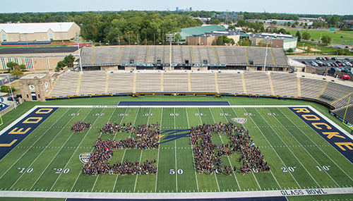 the class of 2028 posed for a photo, forming the an apostrophe and number 28, on the field of Glass Bowl Stadium.