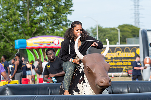 A female UToledo student prepares to ride the mechanical bull at the annual CAP Carnival at Carter Field as part of the 2024 Rocket Welcome Weekend.