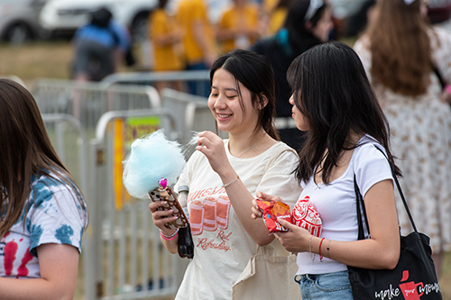 Two female UToledo students enjoy cotton candy and a walking taco at the annual CAP Carnival at Carter Field as part of the 2024 Rocket Welcome Weekend.