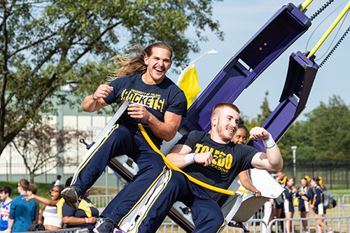 Two male students smile while on a spinning ride at the annual CAP Carnival at Carter Field as part of the 2024 Rocket Welcome Weekend.