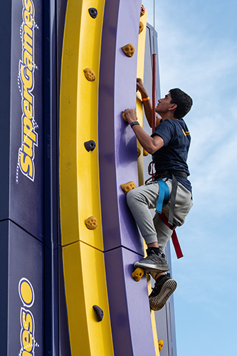 A male UToledo student climbs a rock wall at the annual CAP Carnival at Carter Field as part of the 2024 Rocket Welcome Weekend.