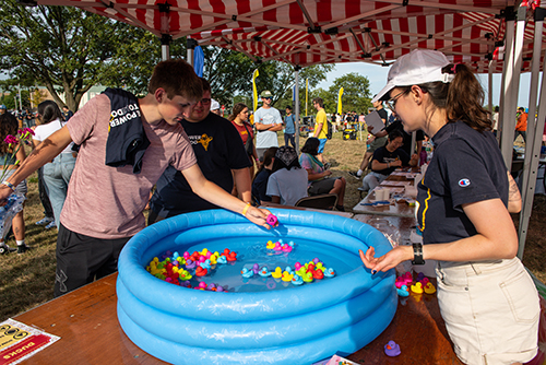 A male UToledo student picks out a colored duck in a small plastic pool at a midway game at the annual CAP Carnival at Carter Field as part of the 2024 Rocket Welcome Weekend.